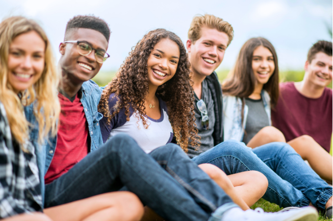 A group of six young people sitting on grass and smiling at the camera.